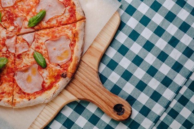 Foto gratuita pizza napolitana con jamón, queso, rúcula, albahaca, tomates espolvoreados con queso sobre una tabla de madera sobre un mantel en una celda con un lugar para el texto