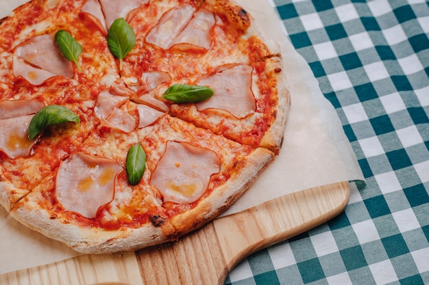 Pizza napolitana con jamón, queso, rúcula, albahaca, tomates espolvoreados con queso sobre una tabla de madera sobre un mantel en una celda