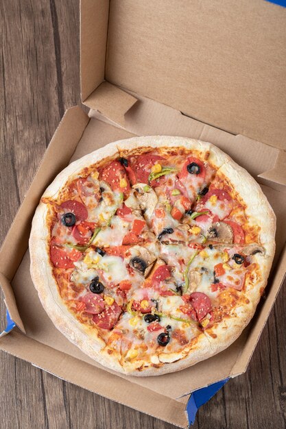 Pizza de pepperoni con aceitunas negras en caja de cartón para llevar