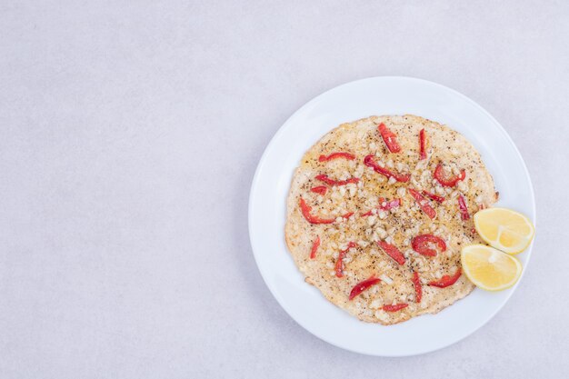 Pizza con pimientos y limón medio cortado en placa blanca sobre blanco