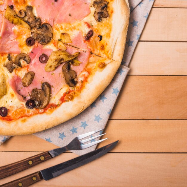 Pizza de queso y champiñones en mesa de madera con tenedor y cuchillo