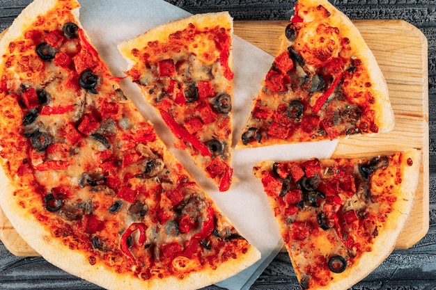 Pizza en rodajas en un primer plano de tablero de pizza sobre un fondo de estuco oscuro