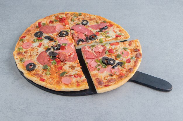 Pizza en rodajas sobre una pizarra negra sobre mármol