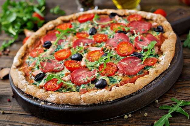 Pizza con salami, tomates, aceitunas y queso sobre una masa con harina integral. Comida italiana.