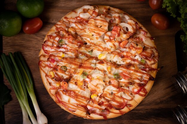Pizza con salchicha, maíz, frijoles, camarones y tocino en una placa de madera