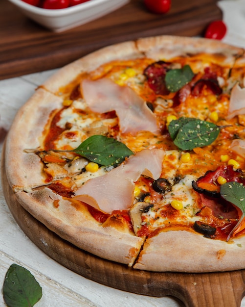 Pizza en salsa de tomate con jamón y albahaca.