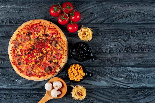 Pizza con tomate, espagueti, maíz, aceitunas, champiñones vista superior sobre un fondo azul oscuro