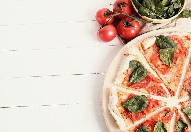 Pizza tradicional con rodajas de tomate y hojas de albahaca