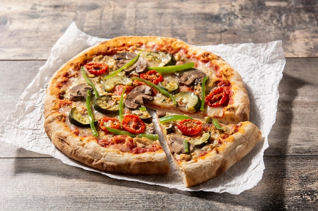 Pizza vegetariana con pimientos de tomate calabacín y champiñones sobre mesa de madera
