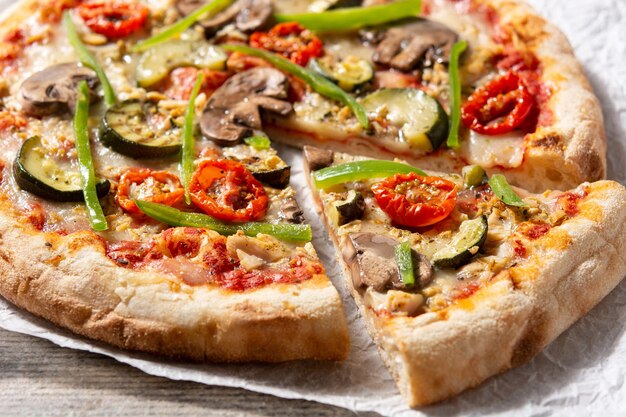 Pizza vegetariana con pimientos de tomate calabacín y champiñones sobre mesa de madera