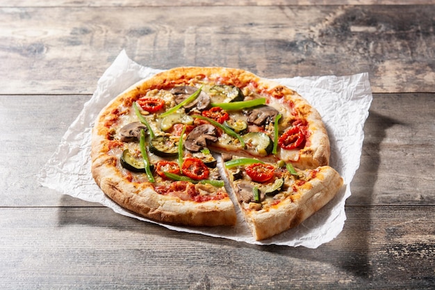 Pizza vegetariana con pimientos de tomate calabacín y champiñones sobre mesa de madera