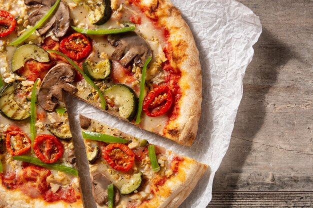 Pizza vegetariana con pimientos de tomate calabacín y champiñones sobre mesa de madera