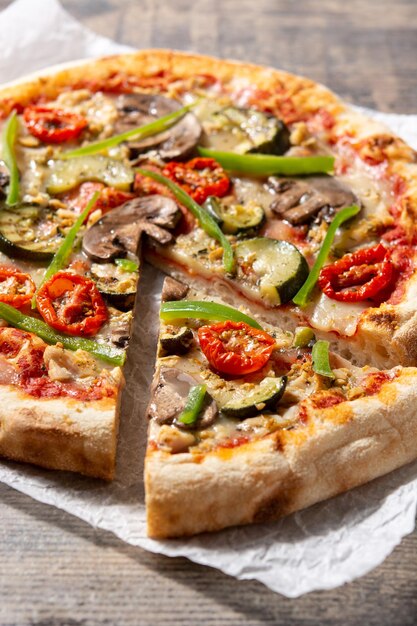 Pizza vegetariana con pimientos de tomate calabacín y champiñones sobre mesa de madera