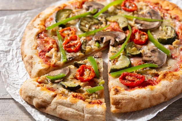 Pizza vegetariana con pimientos de tomate calabacín y champiñones sobre mesa de madera
