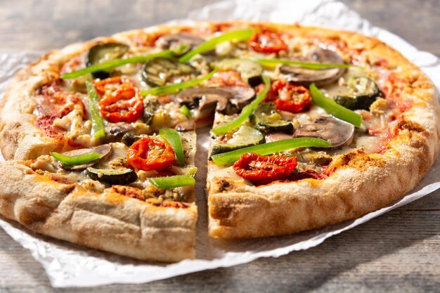 Pizza vegetariana con pimientos de tomate calabacín y champiñones sobre mesa de madera