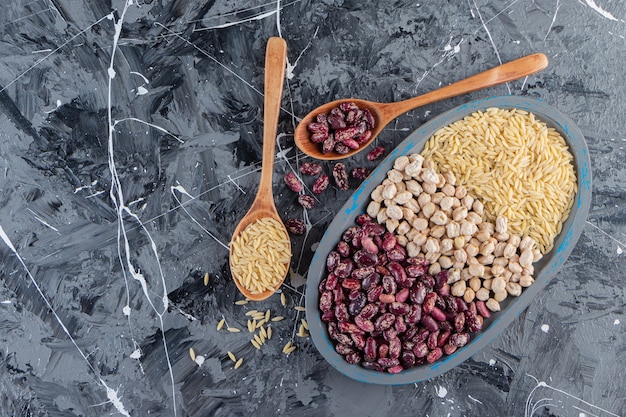 Placa azul llena de garbanzos crudos, arroz y frijoles sobre fondo de mármol.