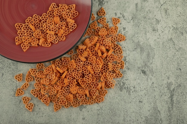 Foto gratuita placa de borgoña de macarrones crudos en forma de corazón sobre fondo de mármol