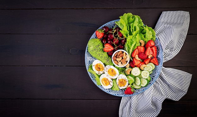 Placa con una dieta de dieta paleo. Huevos cocidos, aguacate, pepino, nueces, cerezas y fresas. Paleo desayuno. Vista superior