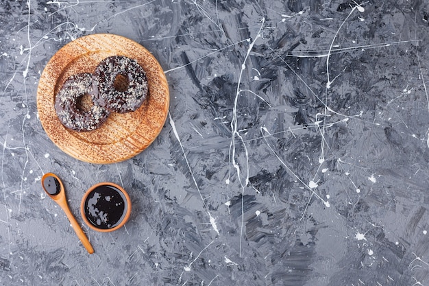 Placa de madera de donas de chocolate con chispitas de coco sobre fondo de mármol.