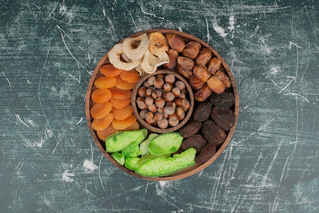 Placa de madera con frutos secos sobre mesa de mármol