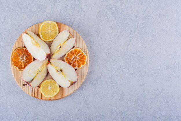 Placa de madera de manzanas frescas y rodajas de limón sobre la mesa de piedra.