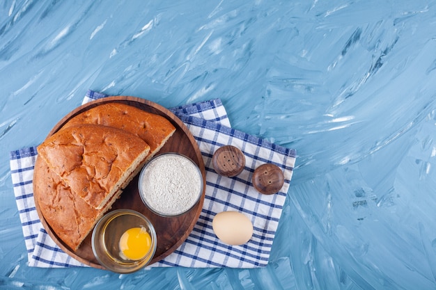 Placa de madera de pan de molde, yema de huevo y harina sobre superficie azul.