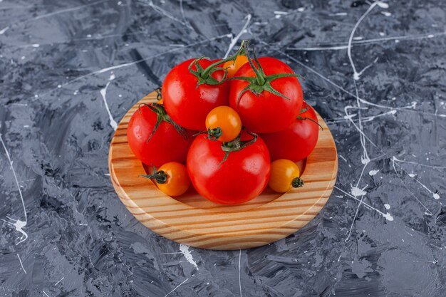 Placa de madera de tomates cherry y rojos sobre superficie de mármol.