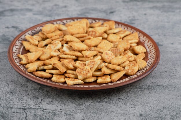 Placa marrón llena de galletas saladas secas en mármol.