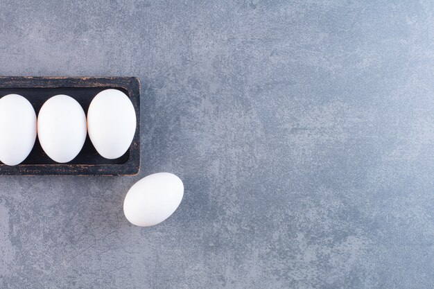 Placa negra de huevos blancos orgánicos en la mesa de piedra.