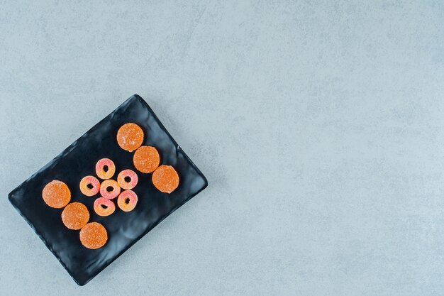 Una placa negra llena de caramelos de gelatina de naranja redondos en forma de anillos y caramelos de gelatina de naranja con azúcar