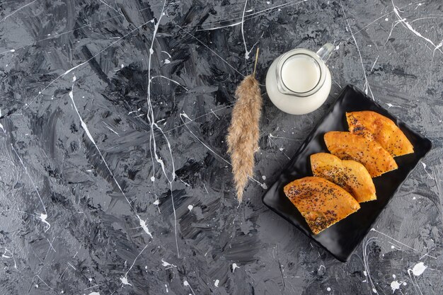 Placa negra de repostería fresca en rodajas y vaso de leche en la mesa de mármol.