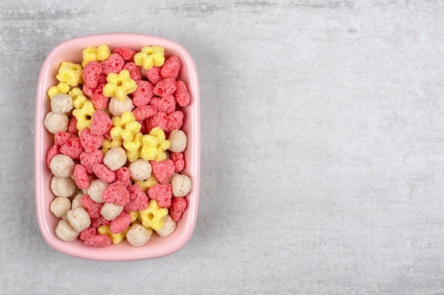 Una placa rosa llena de coloridos cereales para el desayuno colocada sobre una mesa de piedra.