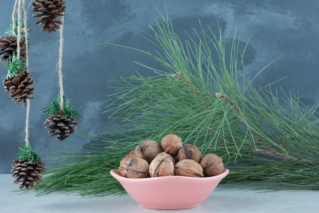 Una placa rosa llena de nueces y piñas de navidad sobre fondo de mármol. foto de alta calidad