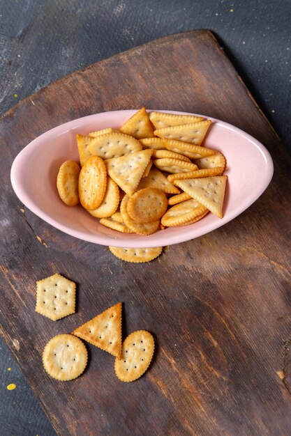 Placa rosa de vista distante superior con galletas y patatas fritas en el escritorio de madera y bocadillo crujiente de galleta de fondo gris