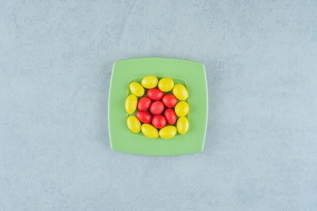 Una placa verde con dulces caramelos amarillos y rojos sobre fondo blanco. Foto de alta calidad