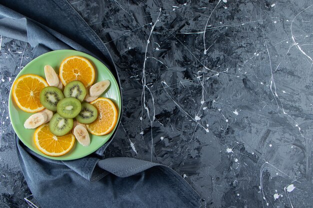 Placa verde de rodajas de naranja, kiwi y plátano sobre superficie de mármol.