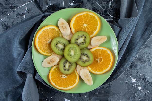 Placa verde de rodajas de naranja, kiwi y plátano sobre superficie de mármol.