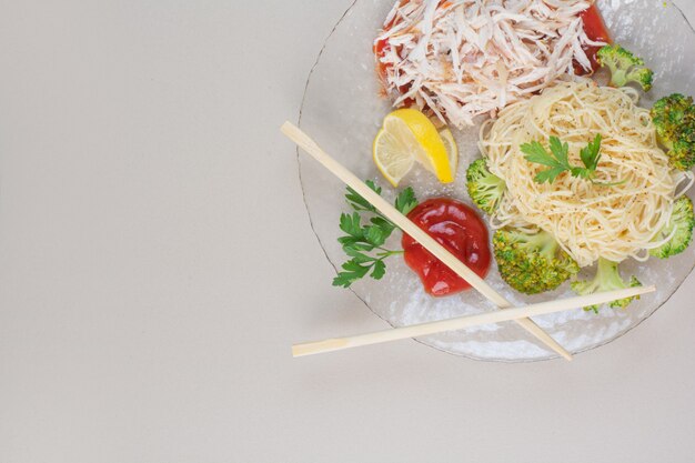 Placa de vidrio de espaguetis, pollo y verduras sobre superficie blanca