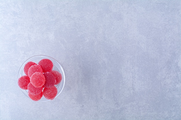 Una placa de vidrio llena de caramelos de gelatina de frutas azucaradas rojas sobre la superficie gris