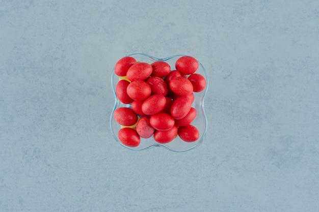 Una placa de vidrio llena de dulces deliciosos caramelos rojos sobre una superficie blanca