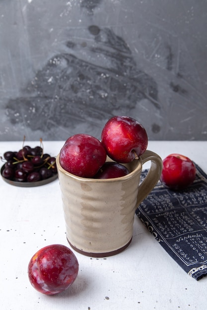 Foto gratuita placa de vista frontal con cerezas oscuras frescas agrias y suaves con ciruelas frescas en gris