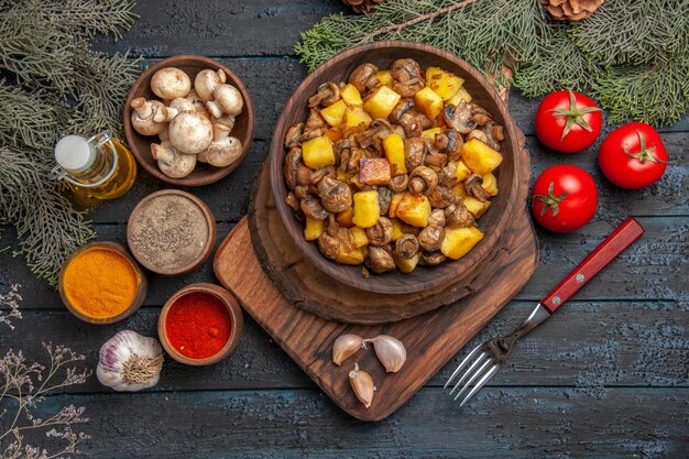 Placa de vista superior cercana y plato de especias de patatas con champiñones en tabla de cortar de madera