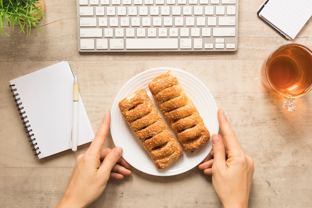 Foto gratuita plana mano que sostiene el plato de hojaldre con notebook