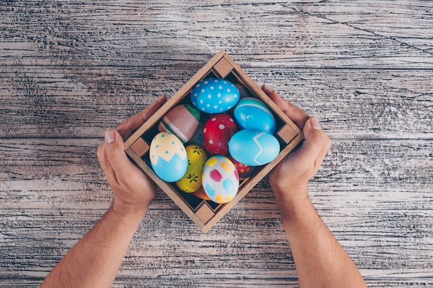 Foto gratuita plana pone huevos de pascua en caja de madera con man_s manos sobre fondo de madera.