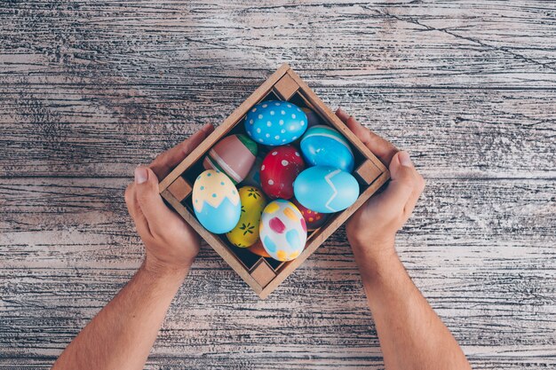 Plana pone huevos de Pascua en caja de madera con man_s manos sobre fondo de madera.