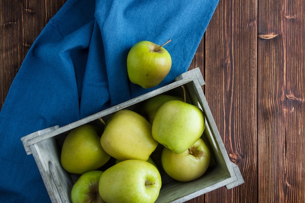 Plana pone manzanas verdes en caja de madera sobre tela azul y fondo de madera. horizontal