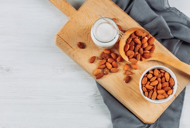 Plana pone tazas de leche con avellanas, almendras y varias nueces sobre fondo blanco de madera. horizontal