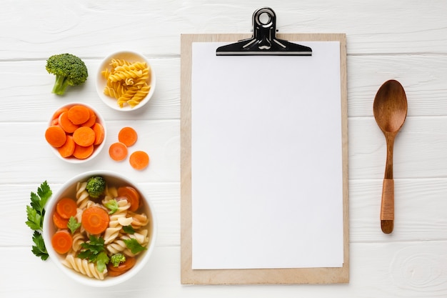 Plana pone zanahorias de brócoli y fusilli en un tazón con cuaderno en blanco