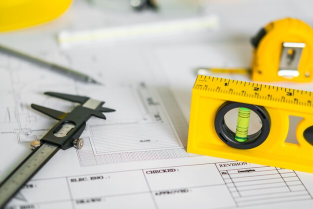 Planes de construcción con casco y herramientas de dibujo en planos.