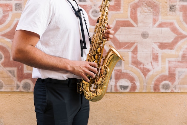 Plano americano de hombre de perfil tocando el saxofón sobre fondo geométrico